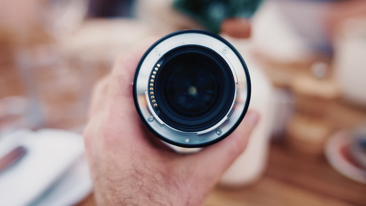 Primo piano dell'obiettivo di una fotocamera tenuto in mano con un effetto bokeh sullo sfondo.
