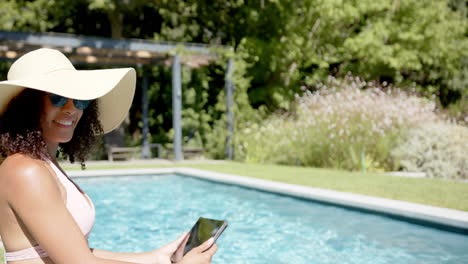 relaxing by pool, woman in sunhat using tablet, enjoying summer day, copy space