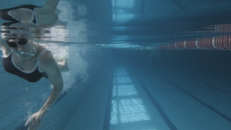 Toma-Submarina-De-Una-Joven-Mujer-Nadando-En-La-Piscina-En-Dirección-A-La-Cámara