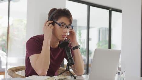 Asian-boy-wearing-headphones-speaking-on-professional-microphone-to-record-audio-podcast-at-home