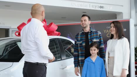 a young family with children inspecting a new car and talking to a dealer at a dealership. a husband and wife are looking at a new luxury model of an electric car. technology and people concept