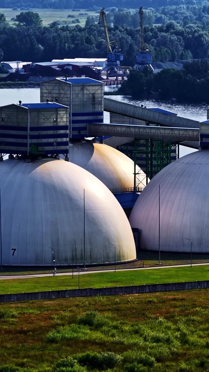 Store industrielle lagerkupler med kraner i baggrunden nær en flod. Ideel til industri- og infrastrukturprojekter