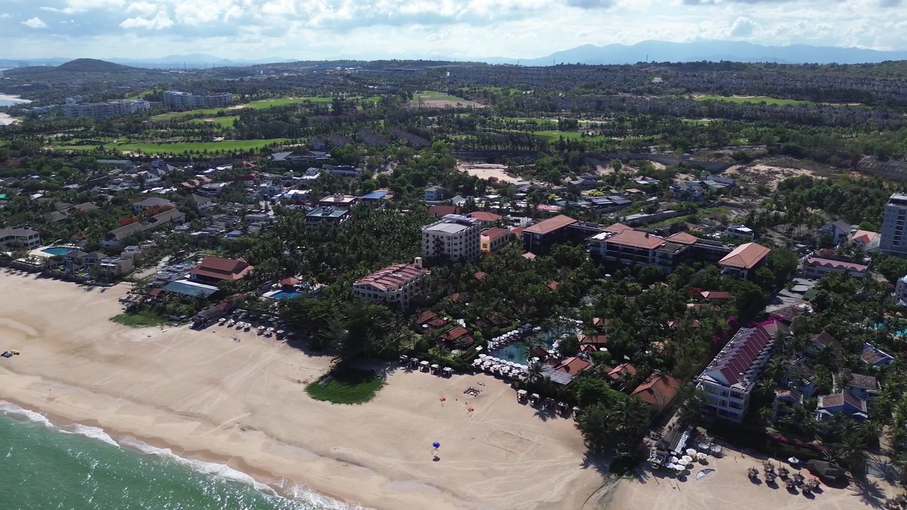 Imágenes de dron de ángulo alto sobre Mui Ne, Vietnam, revelando complejos turísticos frente a la playa, paisajes de palmeras tropicales y una larga costa arenosa, creando una vibrante escena de destino de viaje y turismo en el sudeste asiático.