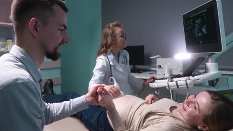 pregnant woman having ultrasound scan at the gynecologist office while loving husband holding her hand 8