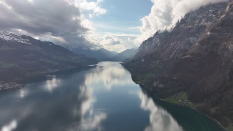 The-stunning-landscape-enveloped-by-towering-mountains,-set-against-a-backdrop-of-sunny-skies-adorned-with-fluffy-clouds