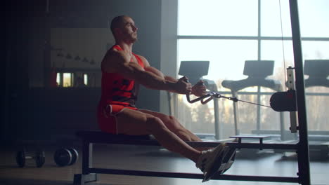 athletic shirtless male doing workouts on a back with power exercise machine in a gym club. side view of muscular man which using rowing machine in gym