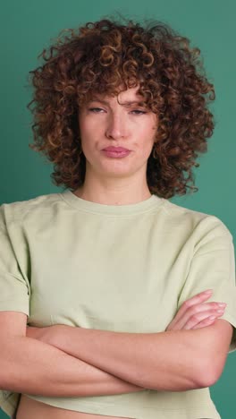 disagreeing young woman shaking head with twisted mouth on green background. vertical orientation