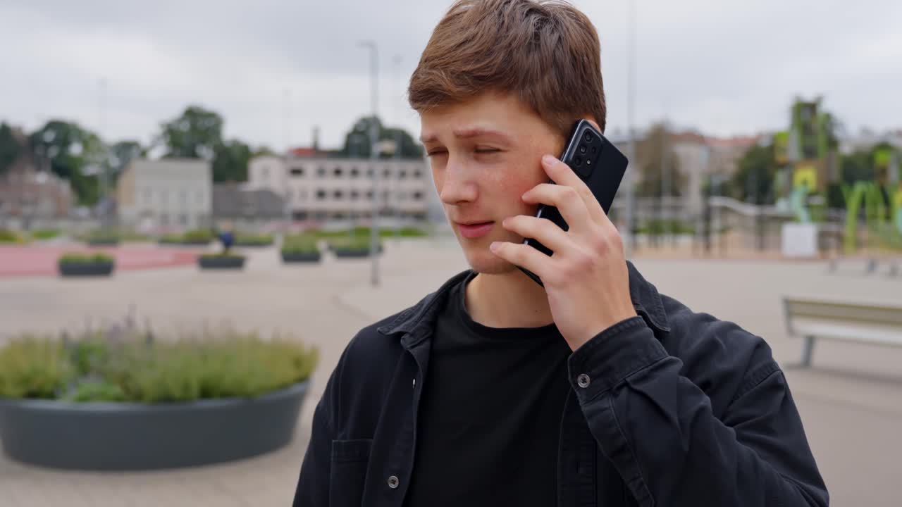 Young man talking on phone during a professional conversation while standing in front square residential area with houses in background