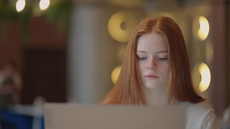Young Red-haired female professional writing an important email from her home. Modern living room. Remote working. serious woman search for inspiration make decision feel lack of ideas