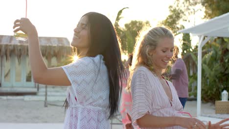 Happy-diverse-group-of-friends-dancing-holding-cocktails-at-beach