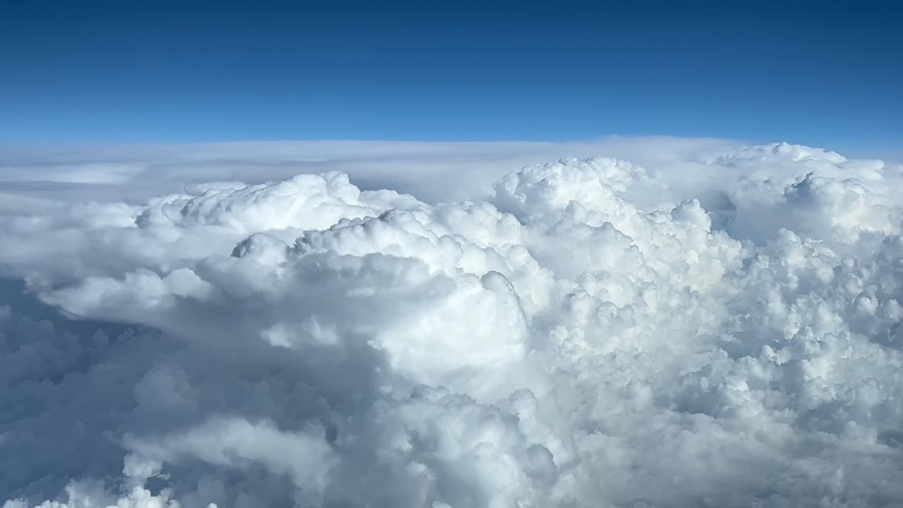 POV pilota - nuvole temporalesche viste dall'alto in un cielo blu, ripreso dalla cabina di pilotaggio di un aereo a quota di crociera FL300.