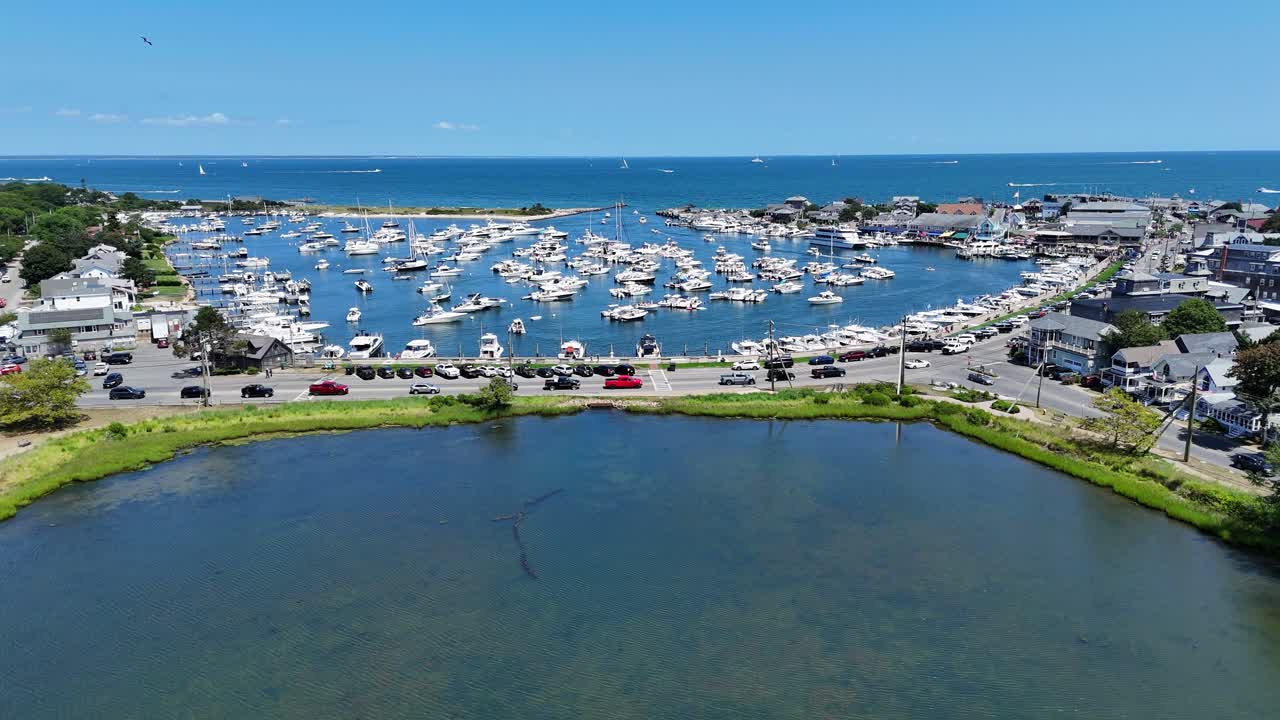 Veduta aerea con drone di Martha’s Vineyard nella contea di Dukes, Massachusetts, con un tranquillo stagno costiero in primo piano e un porto affollato di barche lungo la costa atlantica in una giornata di sole. Ripresa in sorvolo