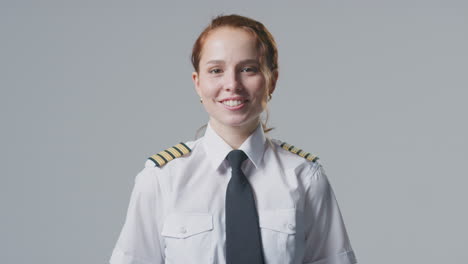 studio portrait of smiling female airline pilot or ship captain against plain background