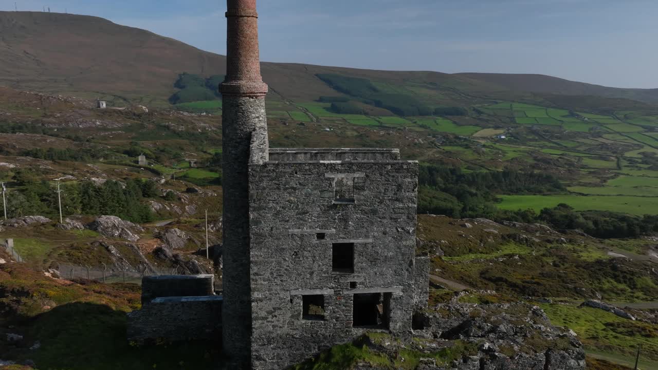 Copper Mine, Allihies, County Cork, Ireland, September 2024. Drone orbits clockwise and pulls backwards away from the stone ruins on the rugged mountain slope under a bright blue sky.