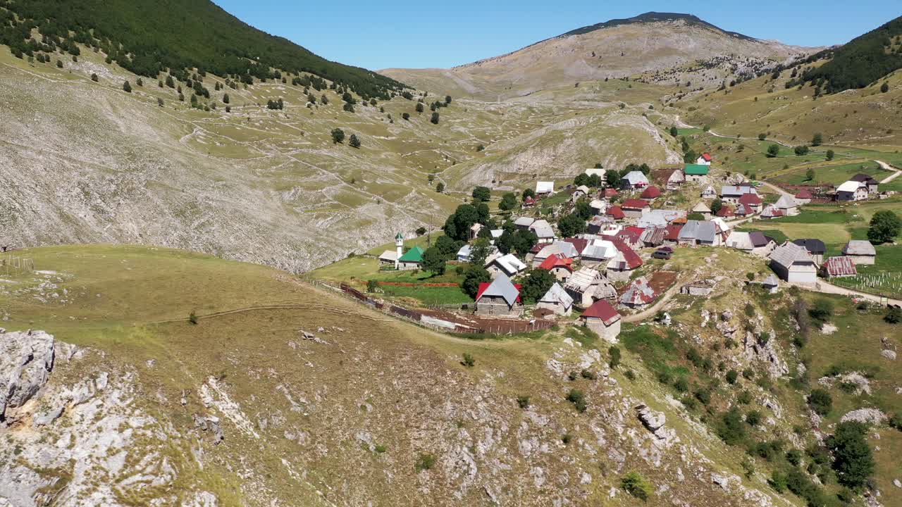 Drone flight along a village on top of a mountain, surrounded by other mountains. Panning shot