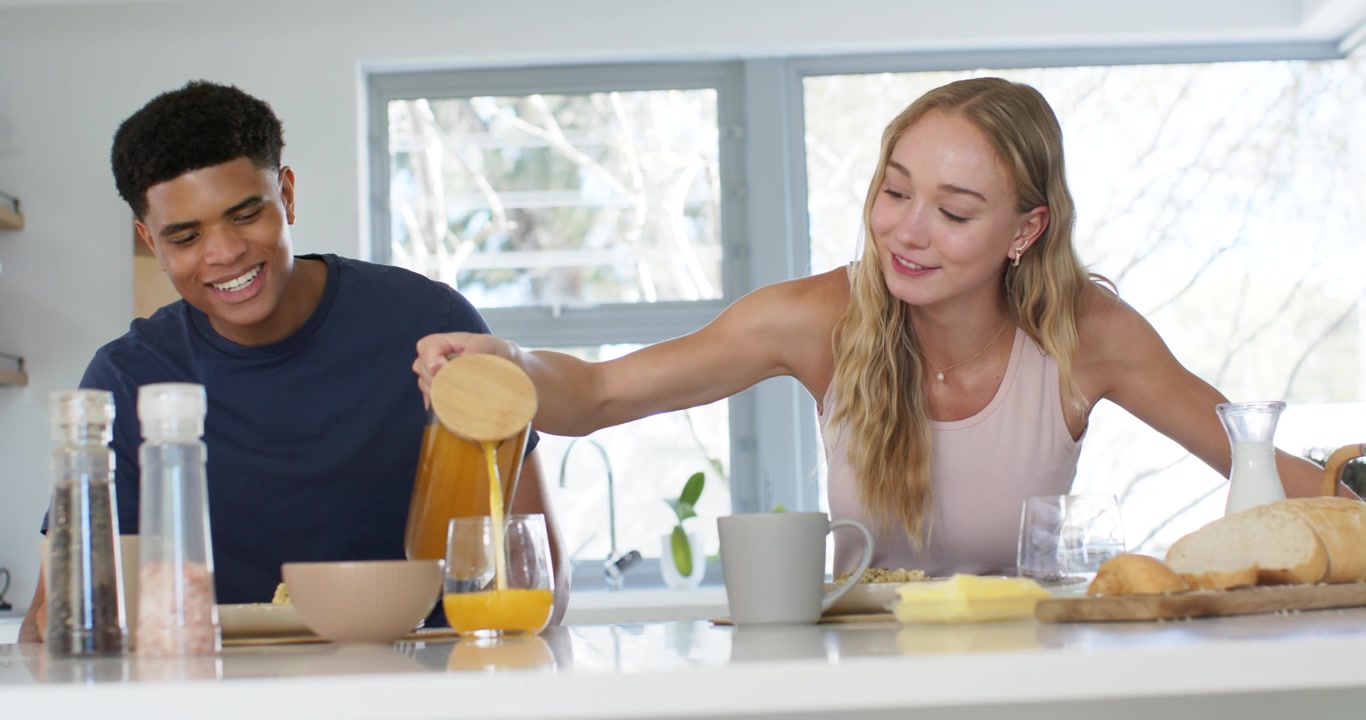 Pareja diversa: mujer sirviendo jugo en el vaso del hombre durante el desayuno en casa.