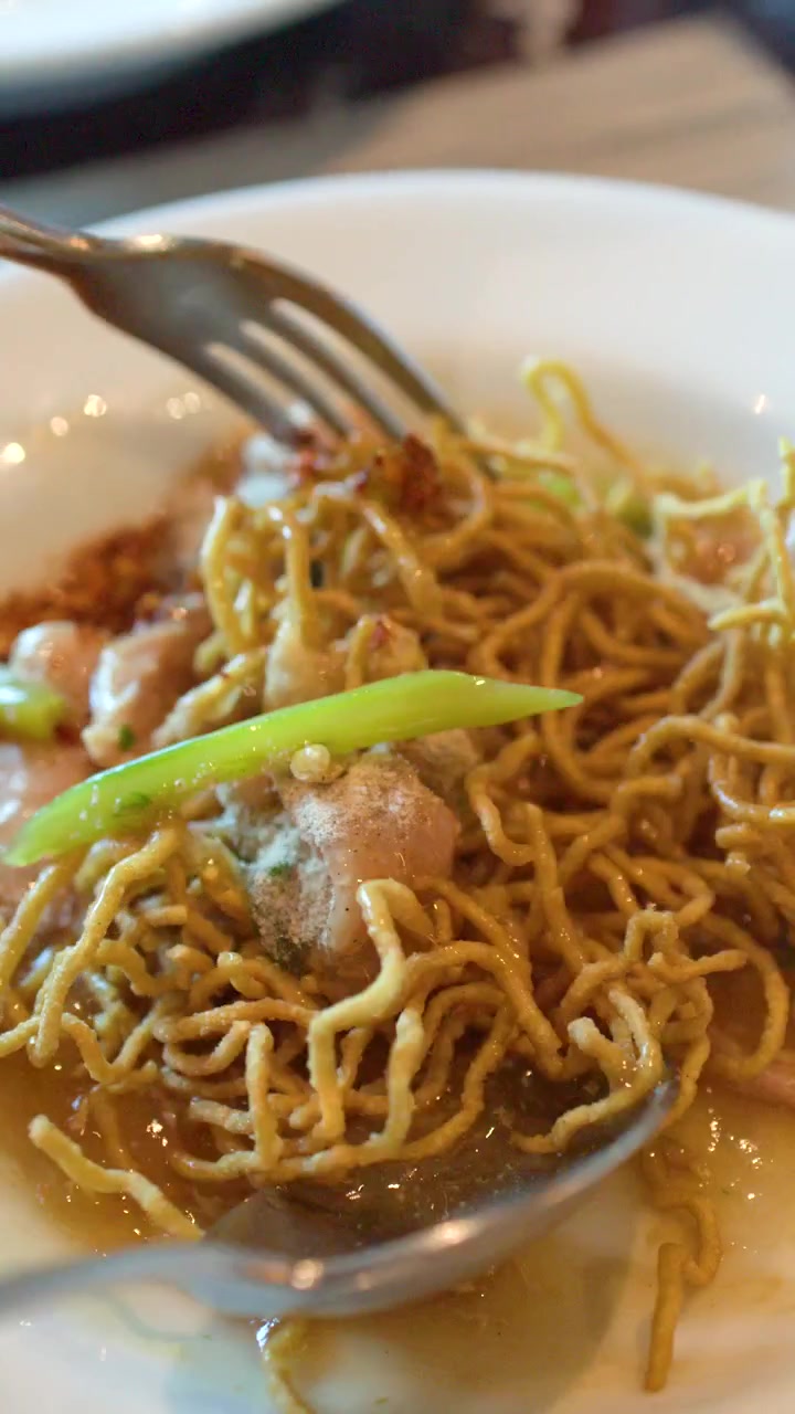 Un primo piano mostra una persona che usa un cucchiaio e una forchetta per mangiare noodles croccanti