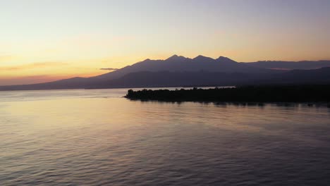 Friedliche-Meereslandschaft-Mit-Violett-gelben-Farben-Des-Himmels-über-Dem-Gebirgshorizont-Und-Der-Silhouette-Einer-Tropischen-Insel-In-Indonesien