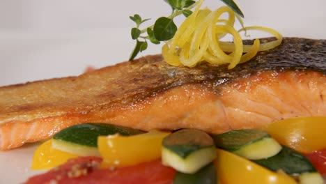 close-up of a grilled salmon fillet with crispy skin served with colorful vegetables and lemon zest