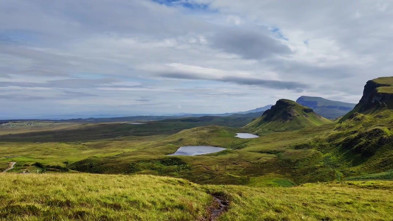 Betagende panorering af en smuk grøn dal set fra Quiraing-bjerget på Isle of Skye, Skotland, på en solrig og blæsende dag