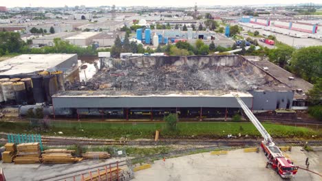 Fire-truck-extinguishes-a-burnt-fuel-warehouse-in-the-industrial-zone,-aerial-view