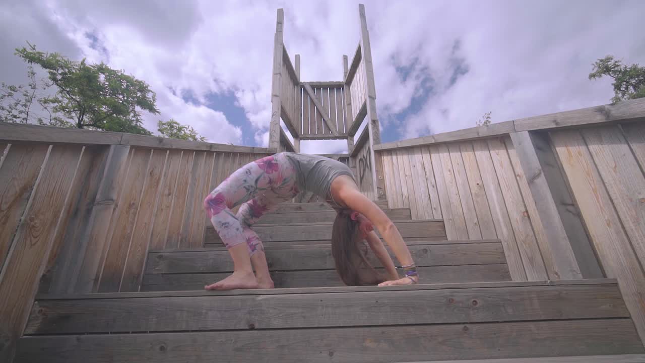 아름 다운 젊은 여자, 야외에서 나무 계단에 바퀴 포즈를 수행