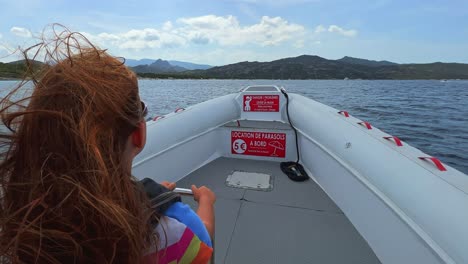 back view of long hair redhead child with sunglasses on motorboat sailing over north corsica sea water for tour toward saleccia famous beach-1