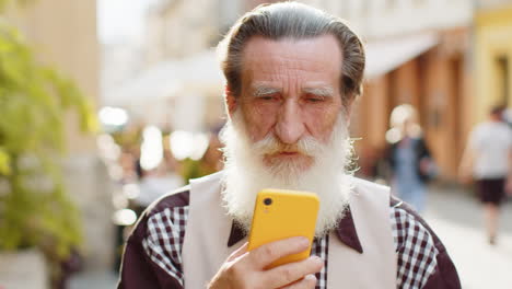senior man use smartphone typing text messages browsing internet finishing work looking at camera