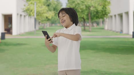 Happy-Indian-boy-scrolling-phone-in-park