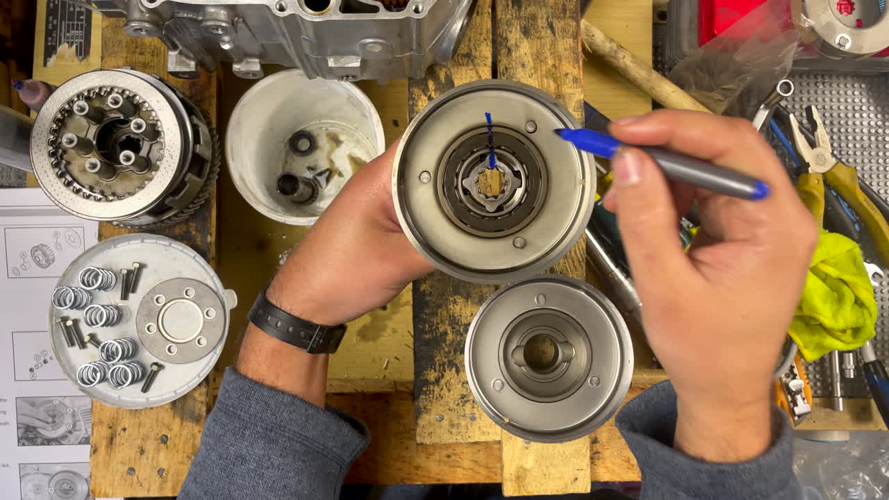 Primo piano di un meccanico che segna l'allineamento della frizione all'interno di una frizione centrifuga con un pennarello blu, garantendo un assemblaggio preciso durante la manutenzione fai-da-te del motore di uno scooter.