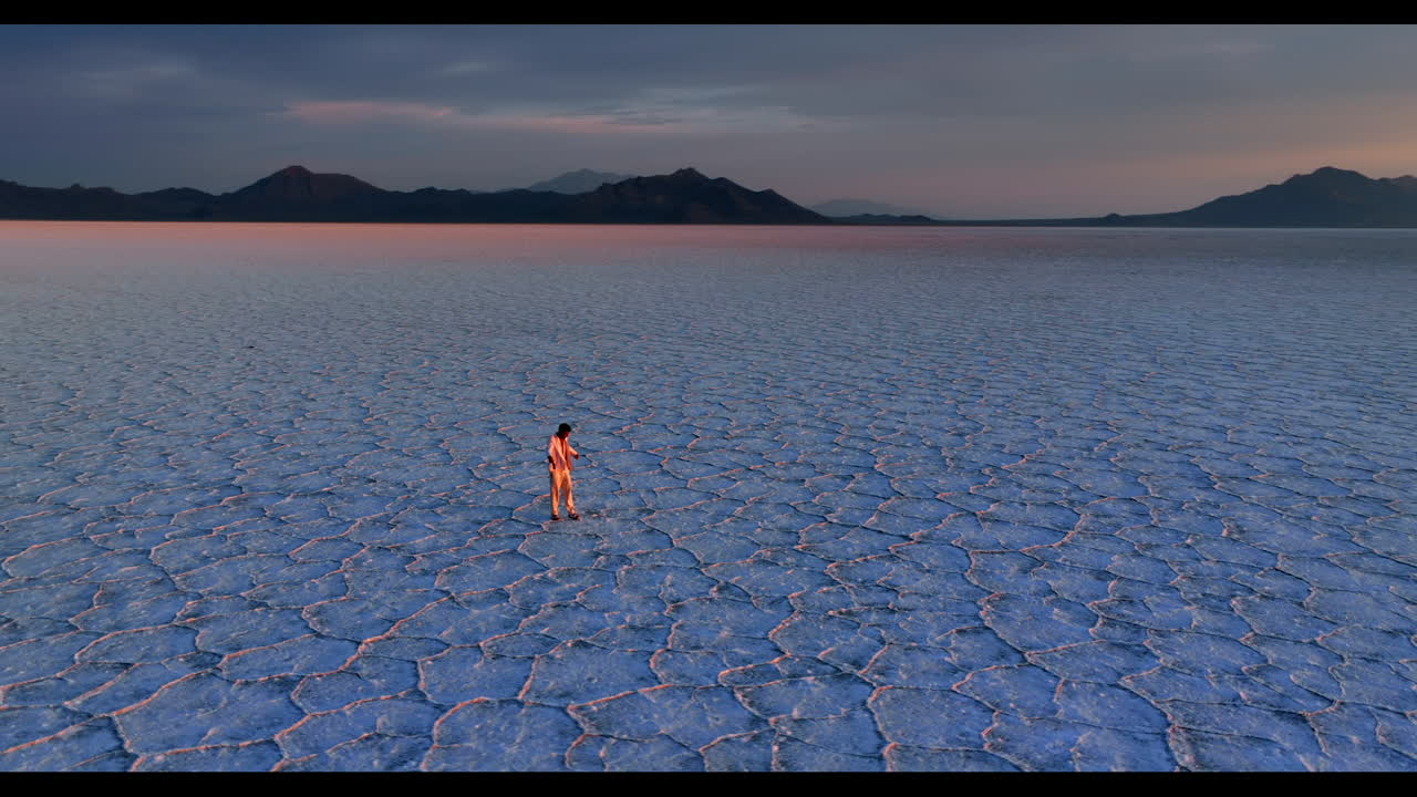 Man in white suit walks by the vast salt pan. Energetic man turns around in the Bonneville Salt Flats, Utah, USA at sunset