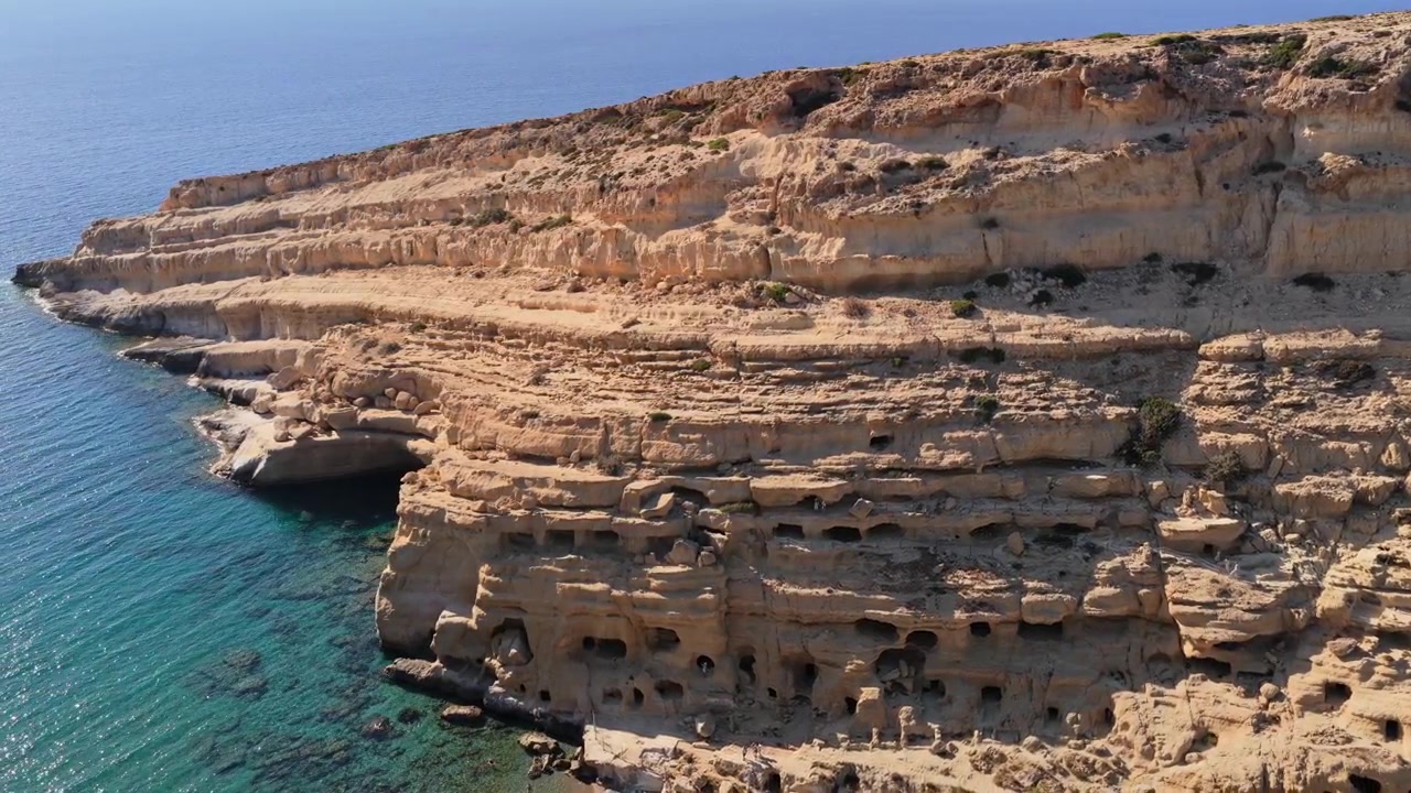 Vista aerea con drone di un promontorio di arenaria a nido d'ape sopra acque limpide e turchesi, Matala, Grecia
