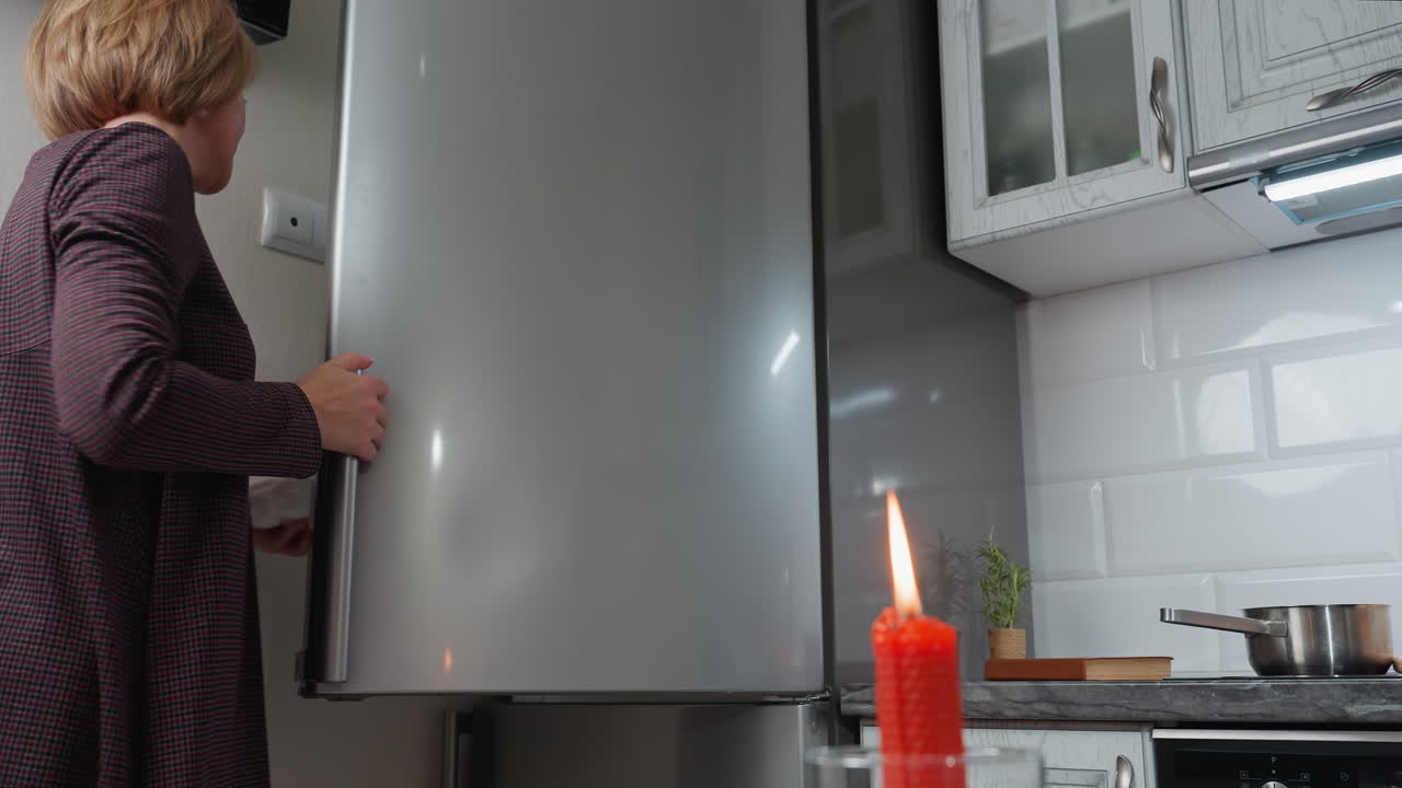 여성이 달 상자를 냉장고에 다시 넣는 동안 부 카운터에 빨간 불이 타고 있습니다. 스테인리스 스 장치, 따뜻한 조명 및 조직 된 카운터탑으로 현대적인 부 설정