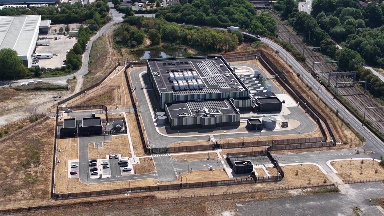 Dronebillede fra høj vinkel af et massivt datacenteranlæg med HVAC-køleenheder, transformerstationer og moderne arkitektur, der driver cloud-netværk og AI-systemer