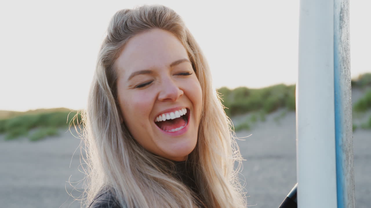 mujer vestida con traje de neopreno sosteniendo una tabla de surf disfrutando de unas vacaciones de surf en la playa mientras el sol se pone