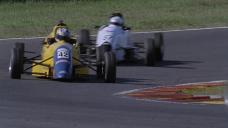 three racing cars round a turn in a racetrack