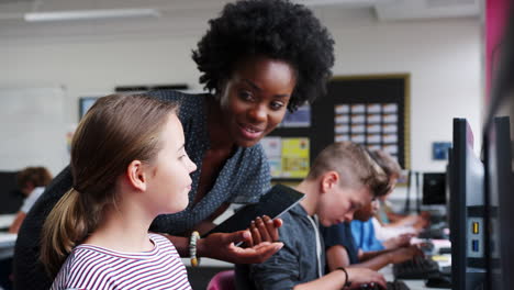 Teacher-Helping-Female-Pupil-In-Line-Of-High-School-Students-Working-at-Screens-In-Computer-Class