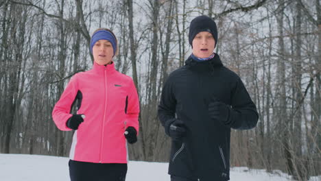un hombre y una mujer jóvenes corren por la mañana en el bosque de invierno. una mujer con una chaqueta holgada y un hombre con una chaqueta negra corre por un parque de invierno. estilo de vida saludable familia feliz.