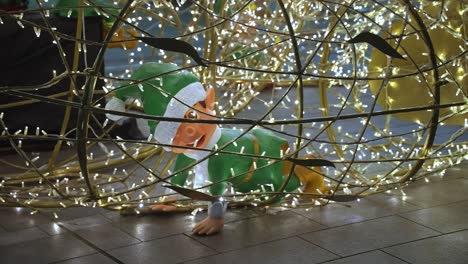 cheeky smiling christmas elf models sat smiling inside a cage of christmas glowing warm fairy lights as foreground and background