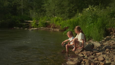 girl and boy throw stones into river playing together in nature. spending summer holidays with family in tourist place without using gadgets for children slow motion