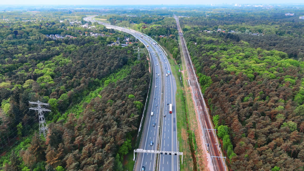 Road and rail in Dutch greenery. Traffic flows along a highway next to a railway surrounded by lush greenery in the Netherlands on a clear day