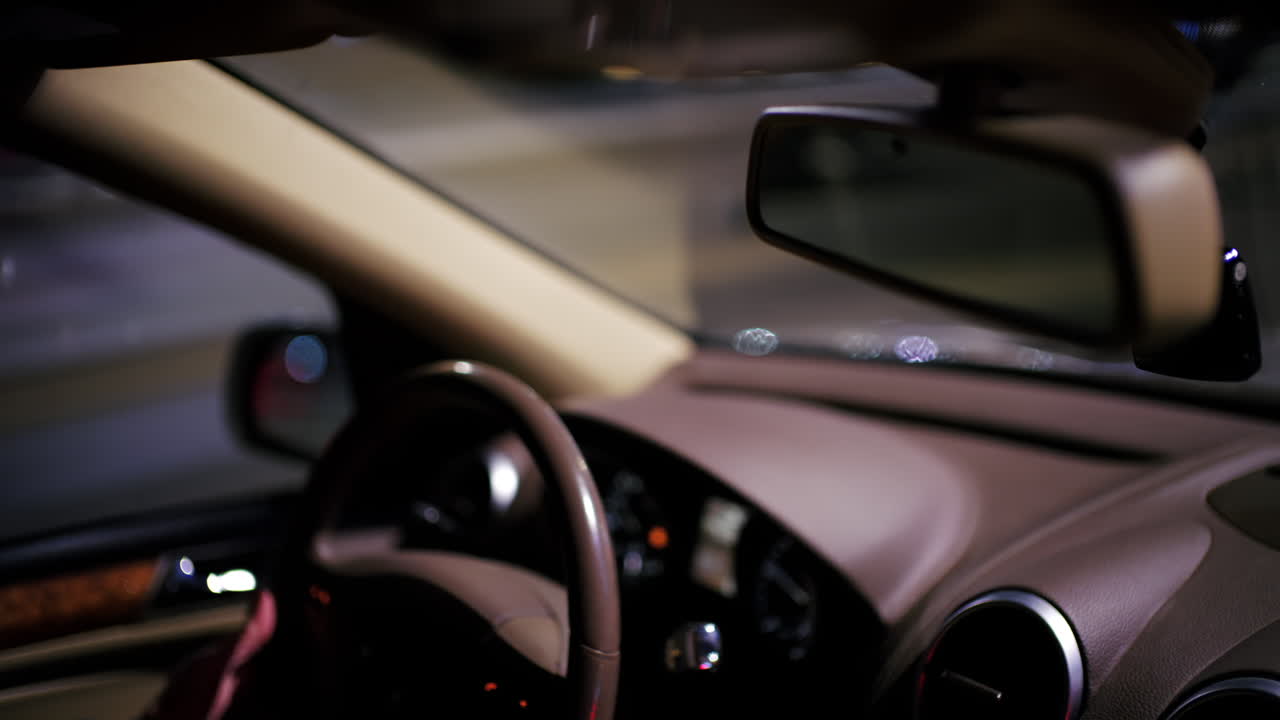 Interno di un'auto ripreso di notte che mostra il cruscotto e lo specchietto retrovisore con luci sfocate della città all'esterno.