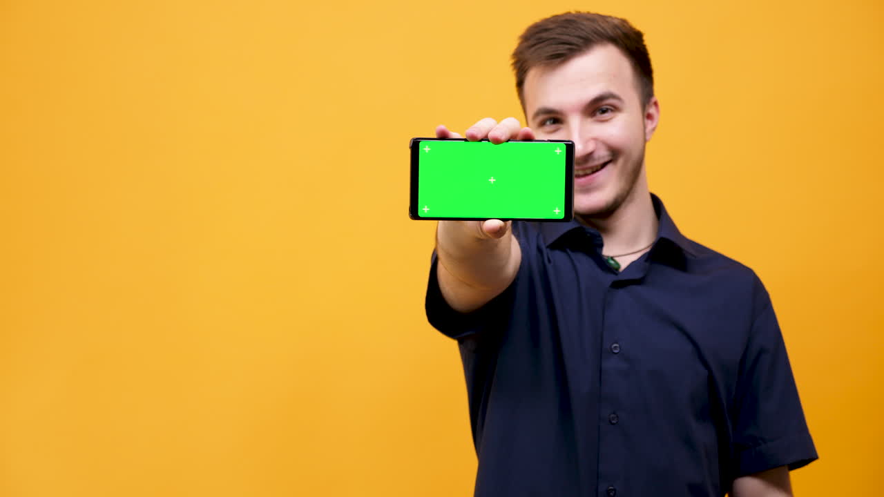 Man holding smartphone with green screen on yellow background