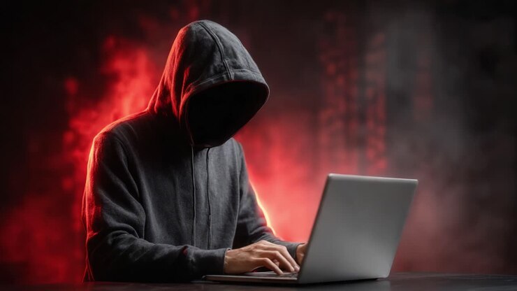 Figura misteriosa con felpa con cappuccio impegnata in attività oscure su un laptop, circondata da inquietante fumo rosso e ombre, che cattura l'essenza di intrighi informatici e segretezza