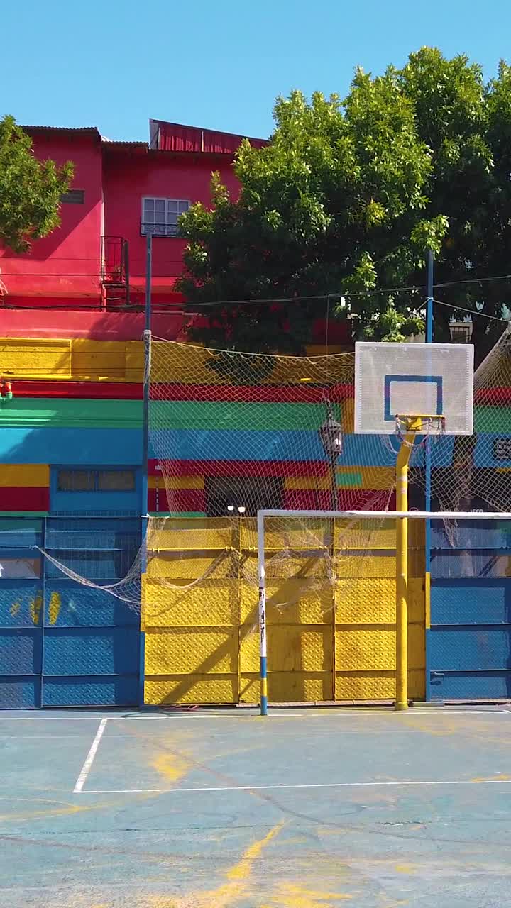 Plaza urbana y fachadas coloridas en Caminito La Boca. Escena vertical de campo de fútbol local, cultura argentina.