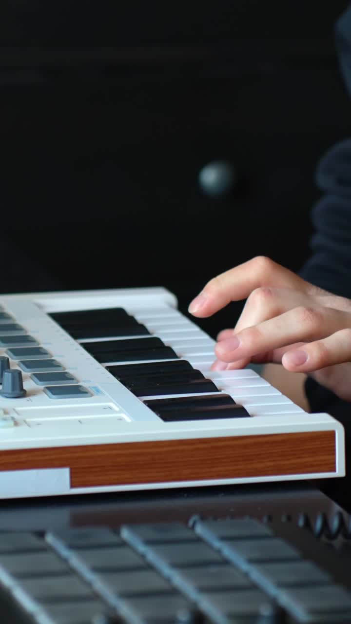 Close-up vertical shot of skilled fingers playing melodic patterns on a white MIDI keyboard in a moody, low-lit home studio