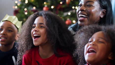 excited children sit on floor with mother as family celebrate christmas together