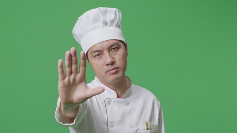 close up of asian man chef looking at camera and disapproving with no hand sign in the green screen background studio