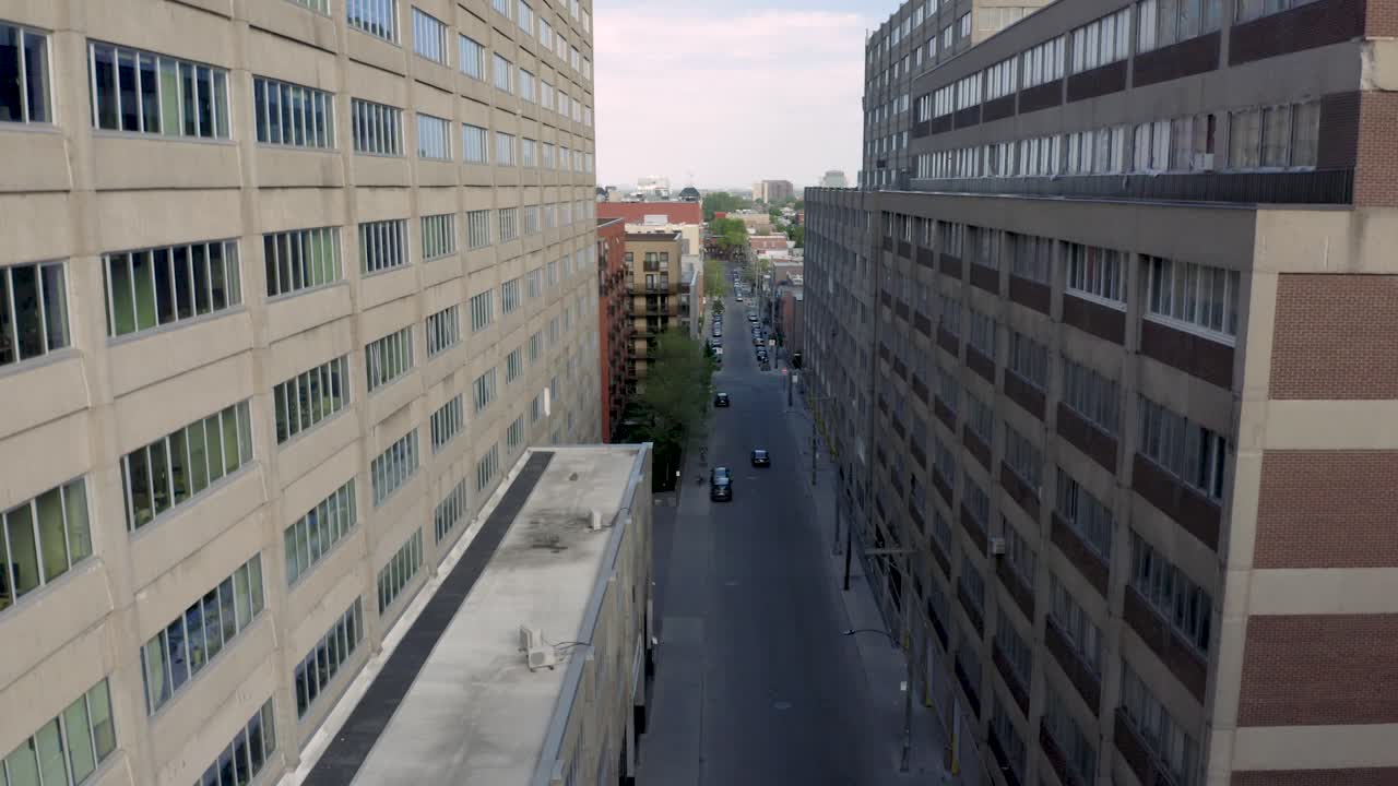 Drone starting in a commercial street where one only car passes by and finishing flying above a sunny day in  Montreal, Quebec, Canada