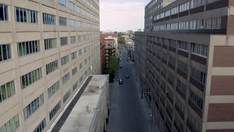 drone starting in a commercial street where one only car passes by and finishing flying above a sunny day in  montreal, quebec, canada